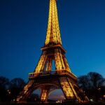 The Eiffel Tower in Paris illuminated at night against a twilight sky, showcasing its iconic iron lattice structure