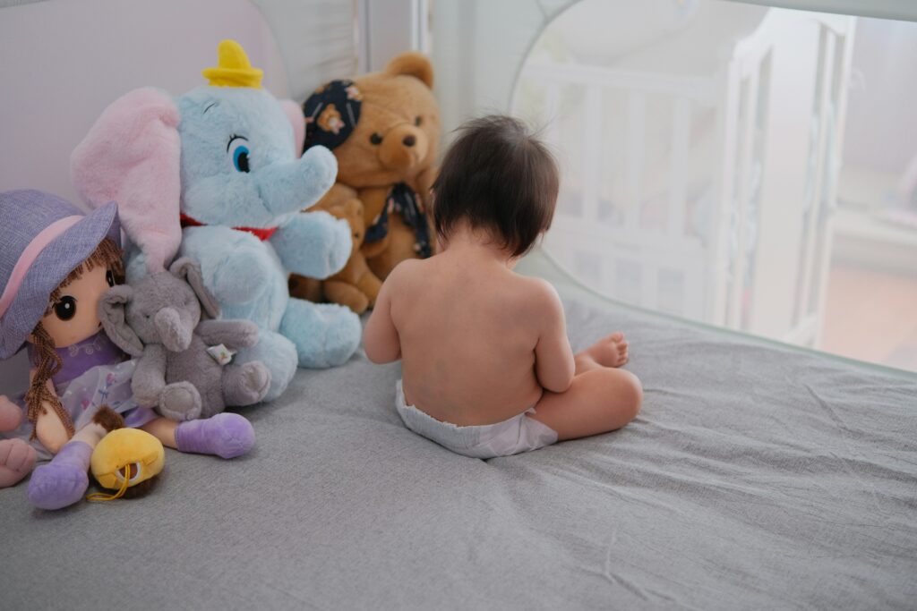 a baby sitting on a bed next to stuffed animals a baby sitting on a bed next to stuffed animals